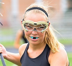 Teen girl playing lacrosse with green mouthguard