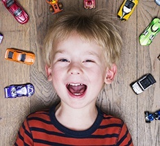 Laughing little boy surrounded by toy cars