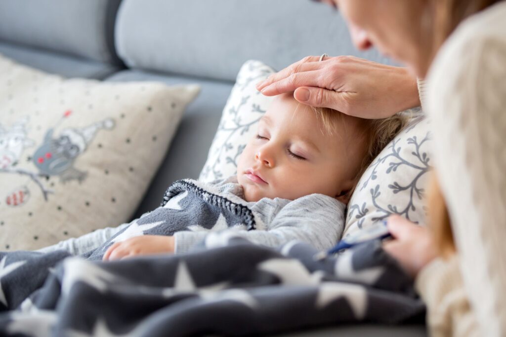 Woman placing hand on sleeping boy's forehead for fever